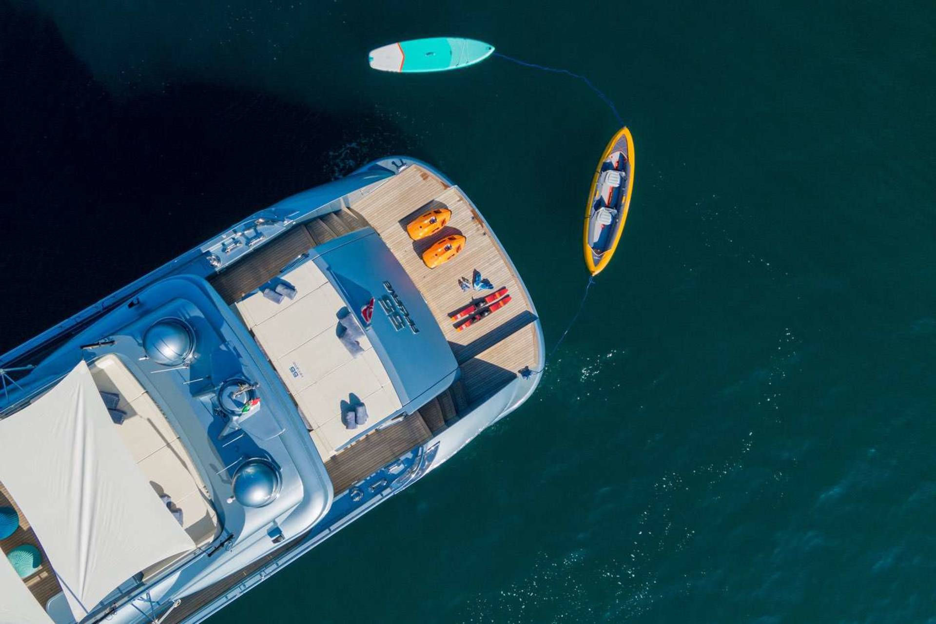 A small boat with a blue and white exterior floats on the dark, deep blue waters, with a yellow kayak visible in the background.