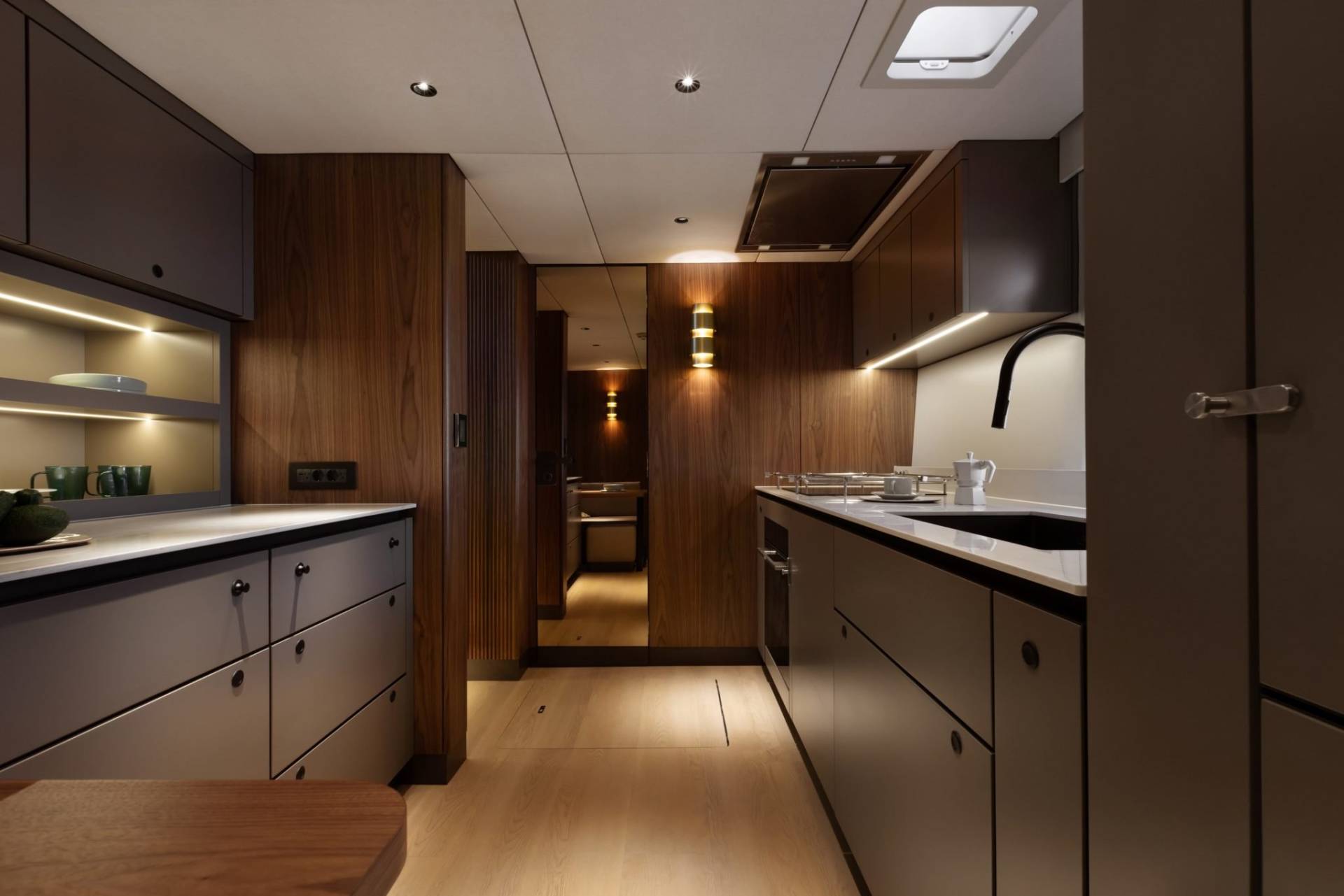 Modern yacht galley features sleek grey cabinetry, warm wood paneling, and integrated lighting for a sophisticated ambiance.