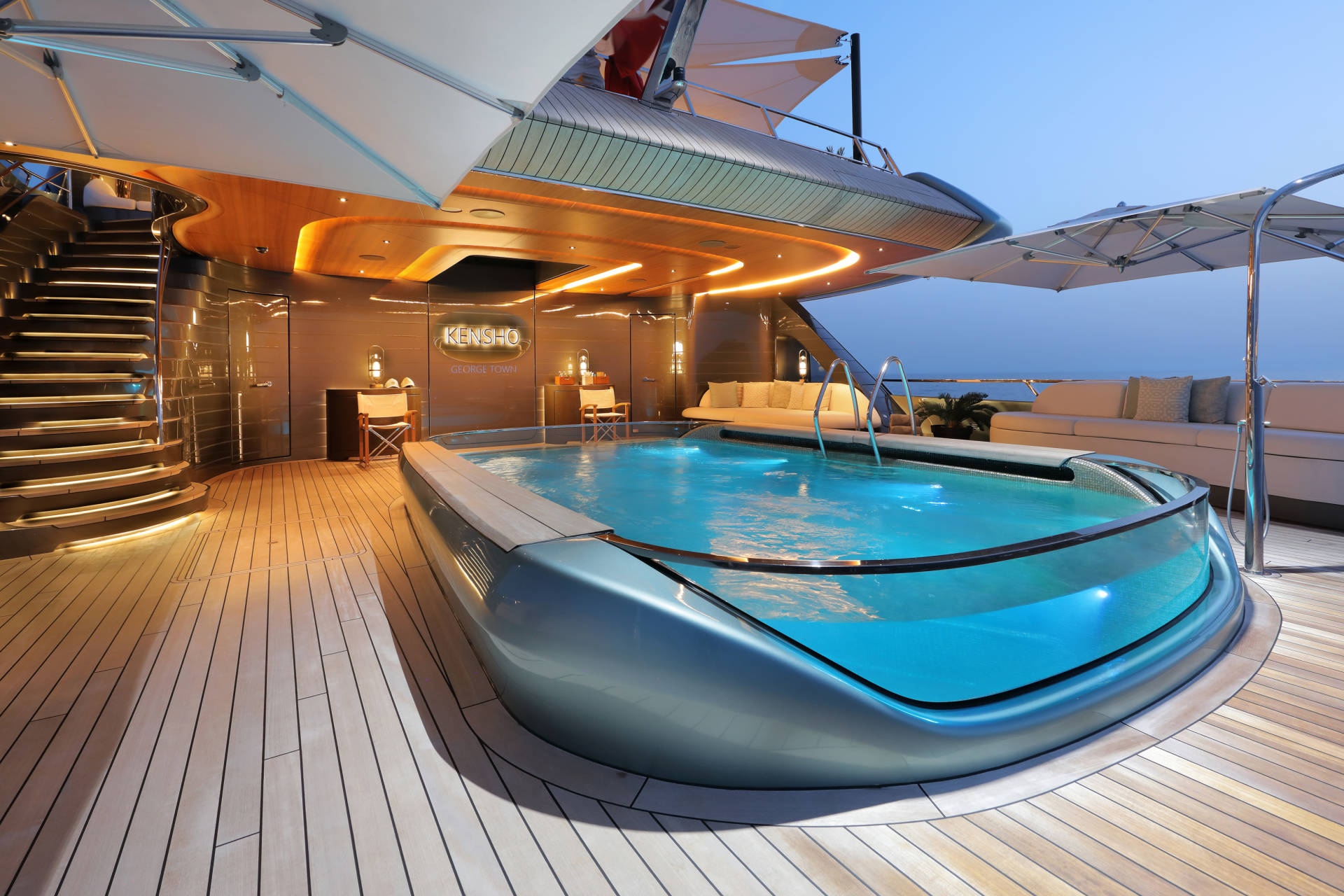 Luxurious yacht deck features a stunning illuminated swimming pool and elegant wooden stairs at twilight.