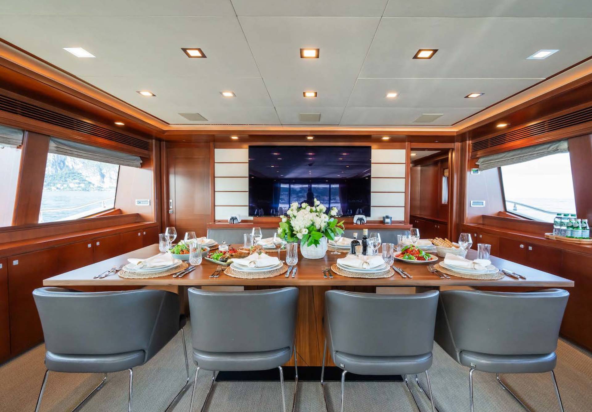 A beautifully set dining table on a yacht awaits guests with a fresh floral centerpiece and stunning views of the water.