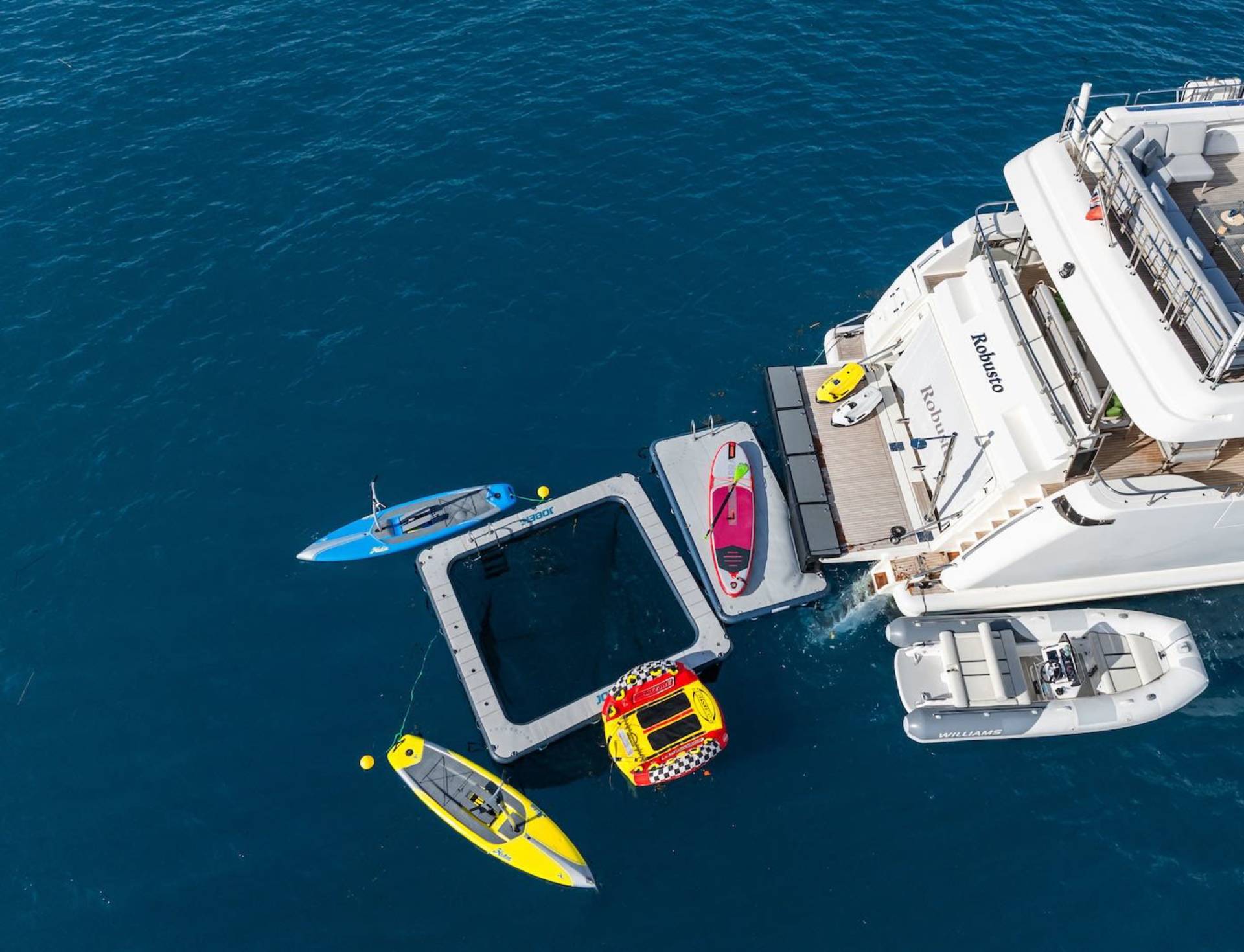 A luxurious yacht floats in the azure sea, surrounded by inflatable toys and watercraft for ultimate aquatic adventure.