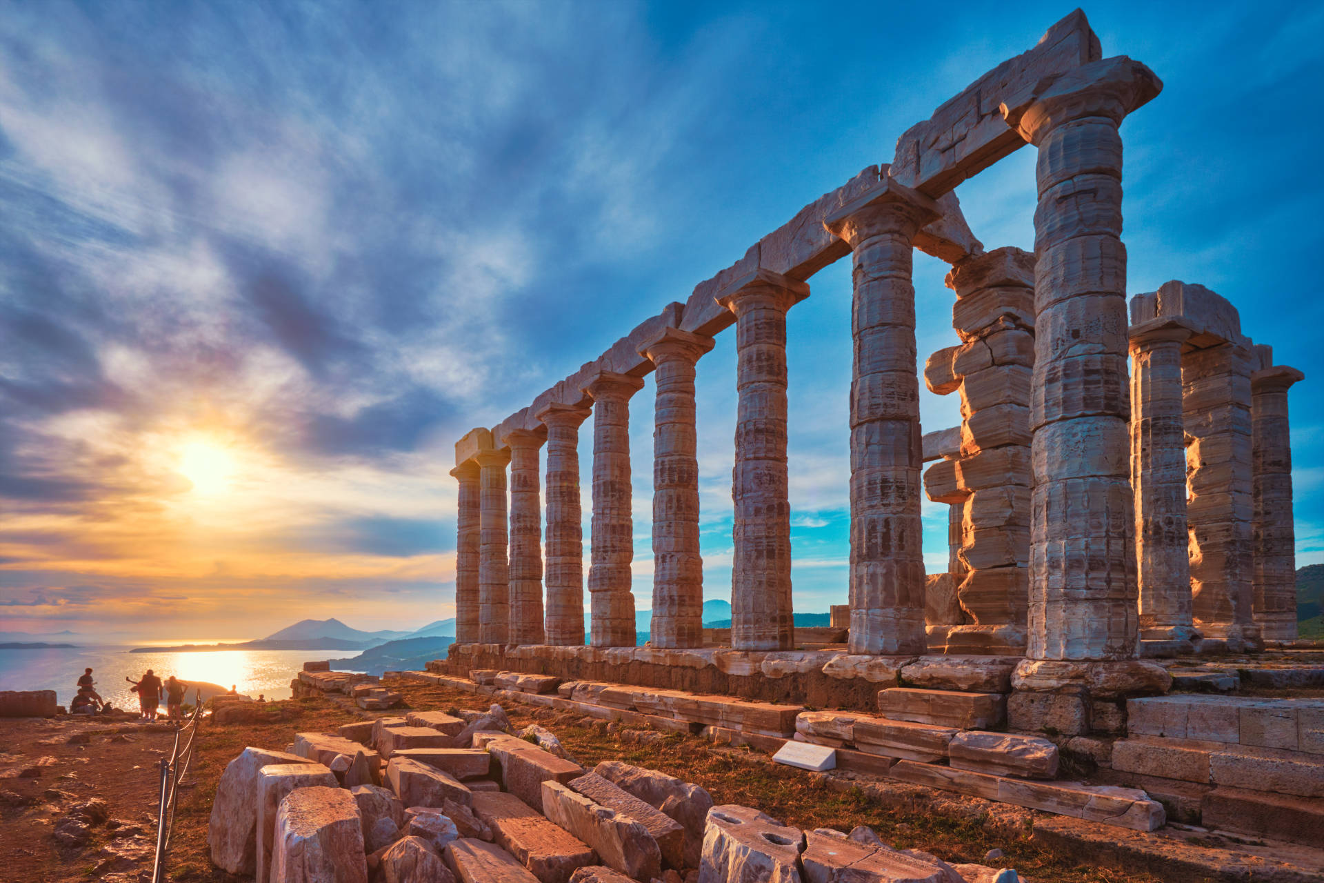 Ancient Greek temple ruins stand majestically against a dramatic sunset over the Aegean Sea.