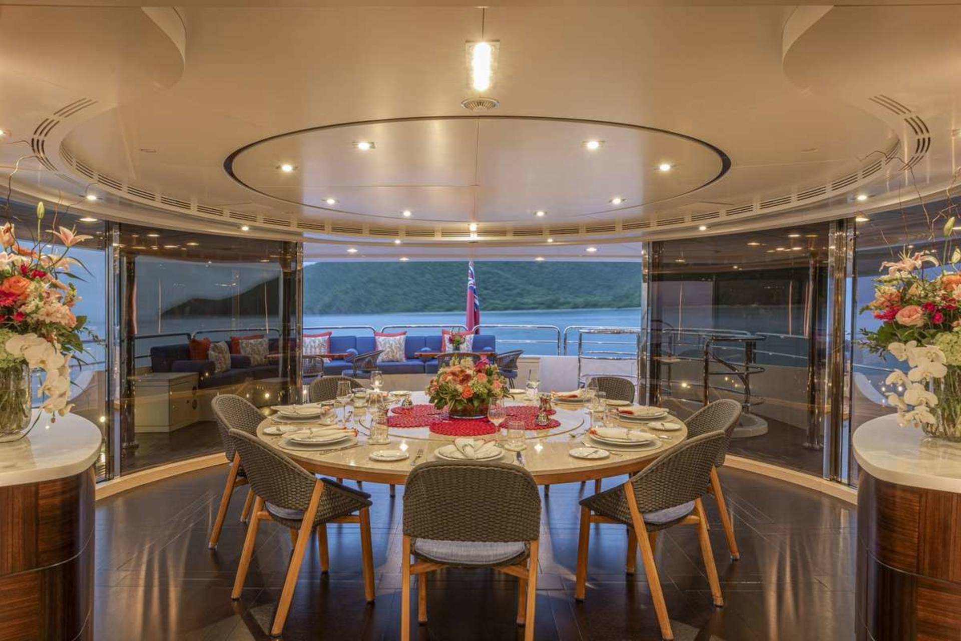 An elegant yacht dining room is set for a formal meal with a stunning view of the ocean and surrounding landscape.