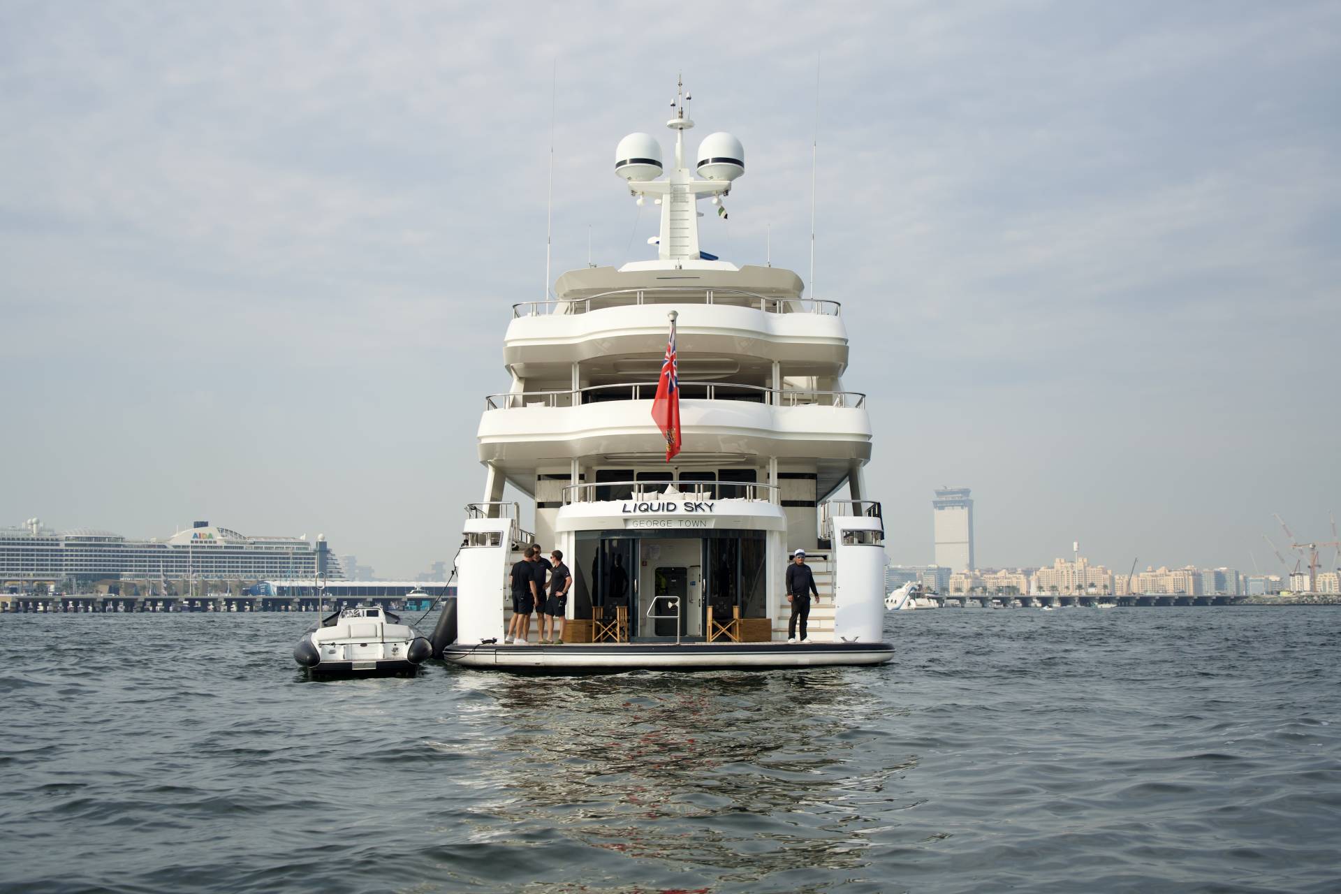 A grand yacht named Liquid Sky is docked in a harbor with a city skyline in the background.