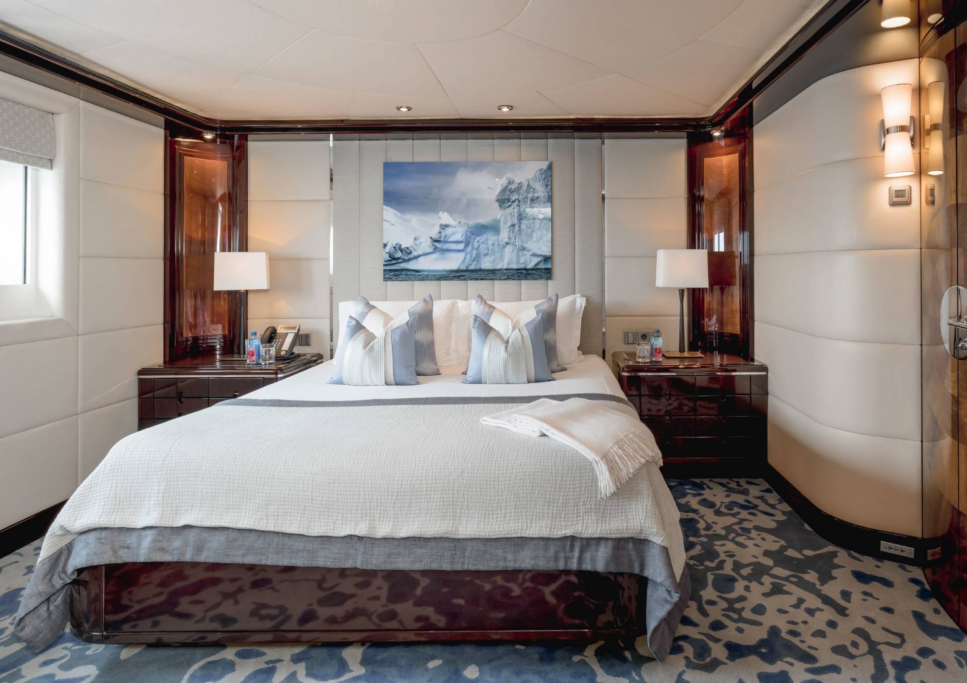 A luxurious yacht cabin features a plush bed adorned with ice-themed artwork and elegant lighting.
