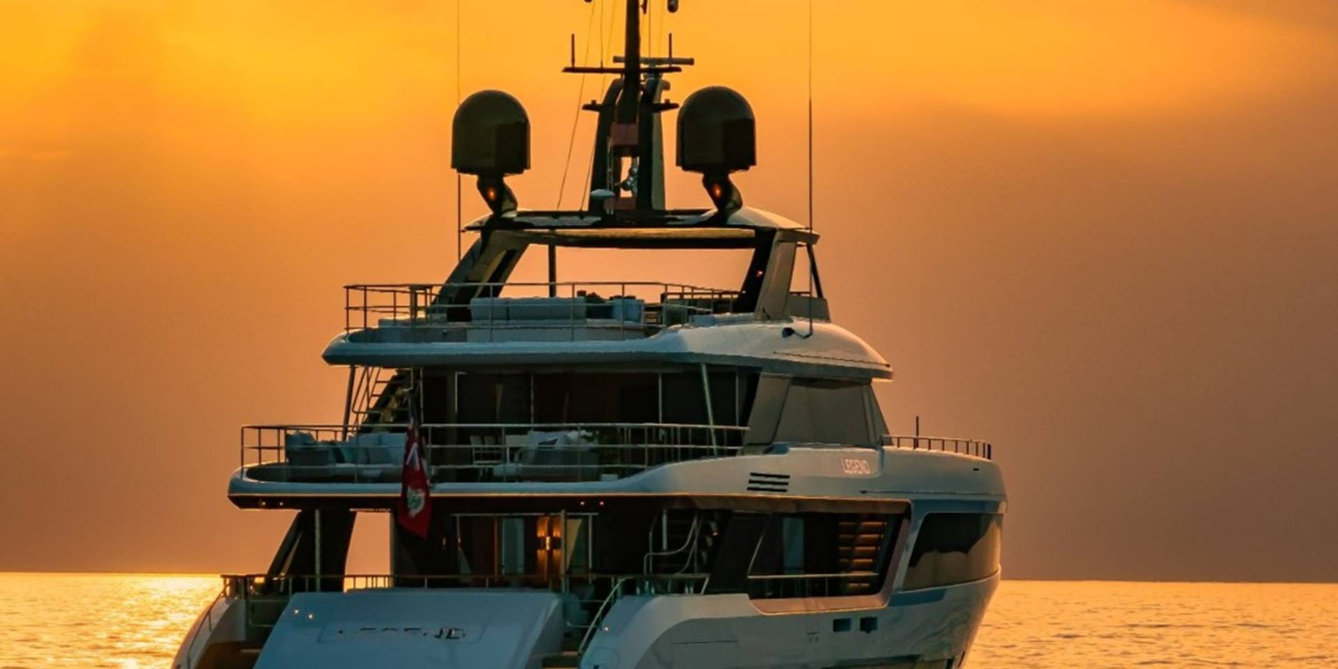 A luxurious yacht glides across the golden ocean waters at sunset.