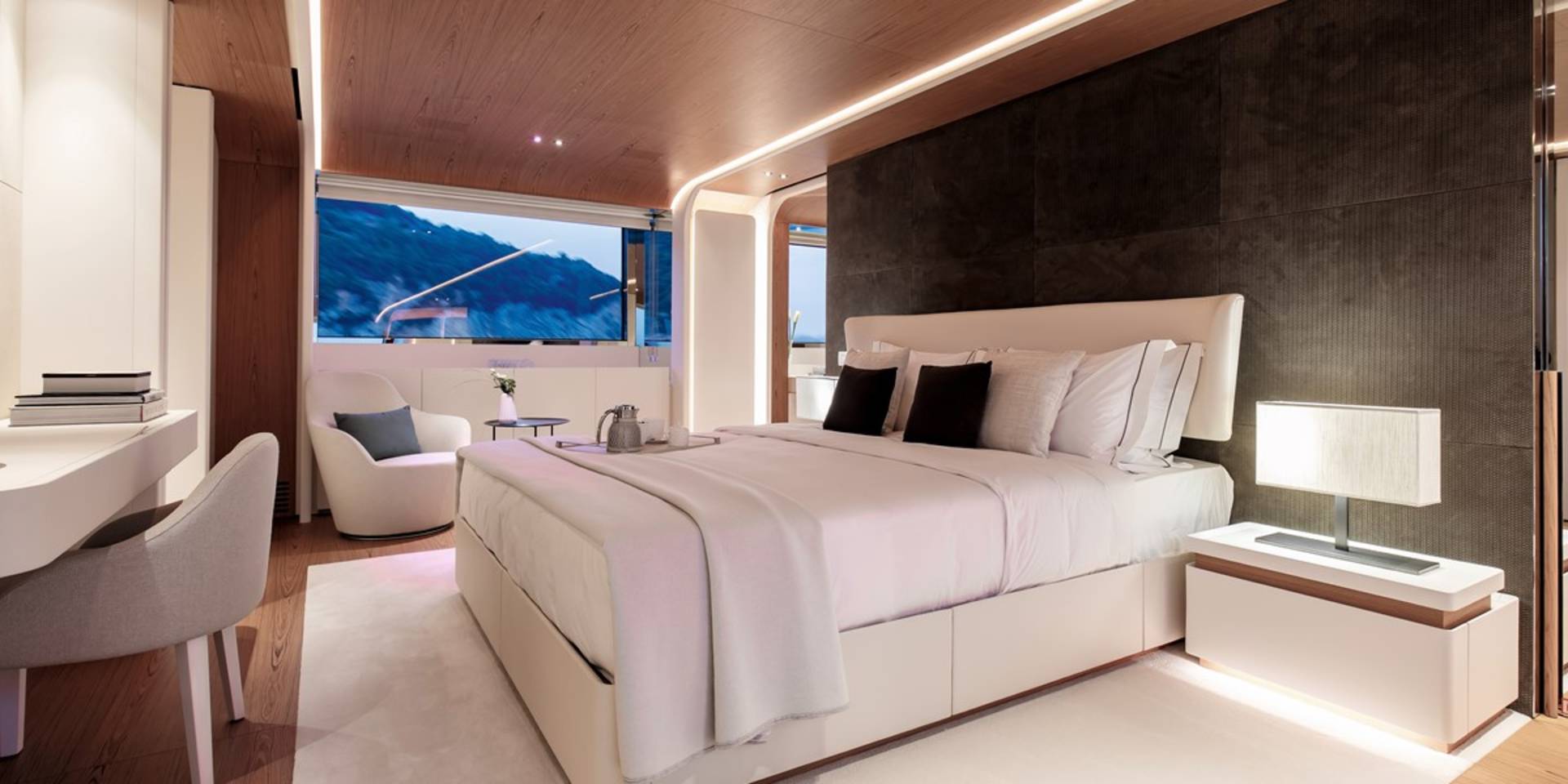 Luxurious yacht bedroom features a king-sized bed, modern desk, and stunning ocean views through a panoramic window.