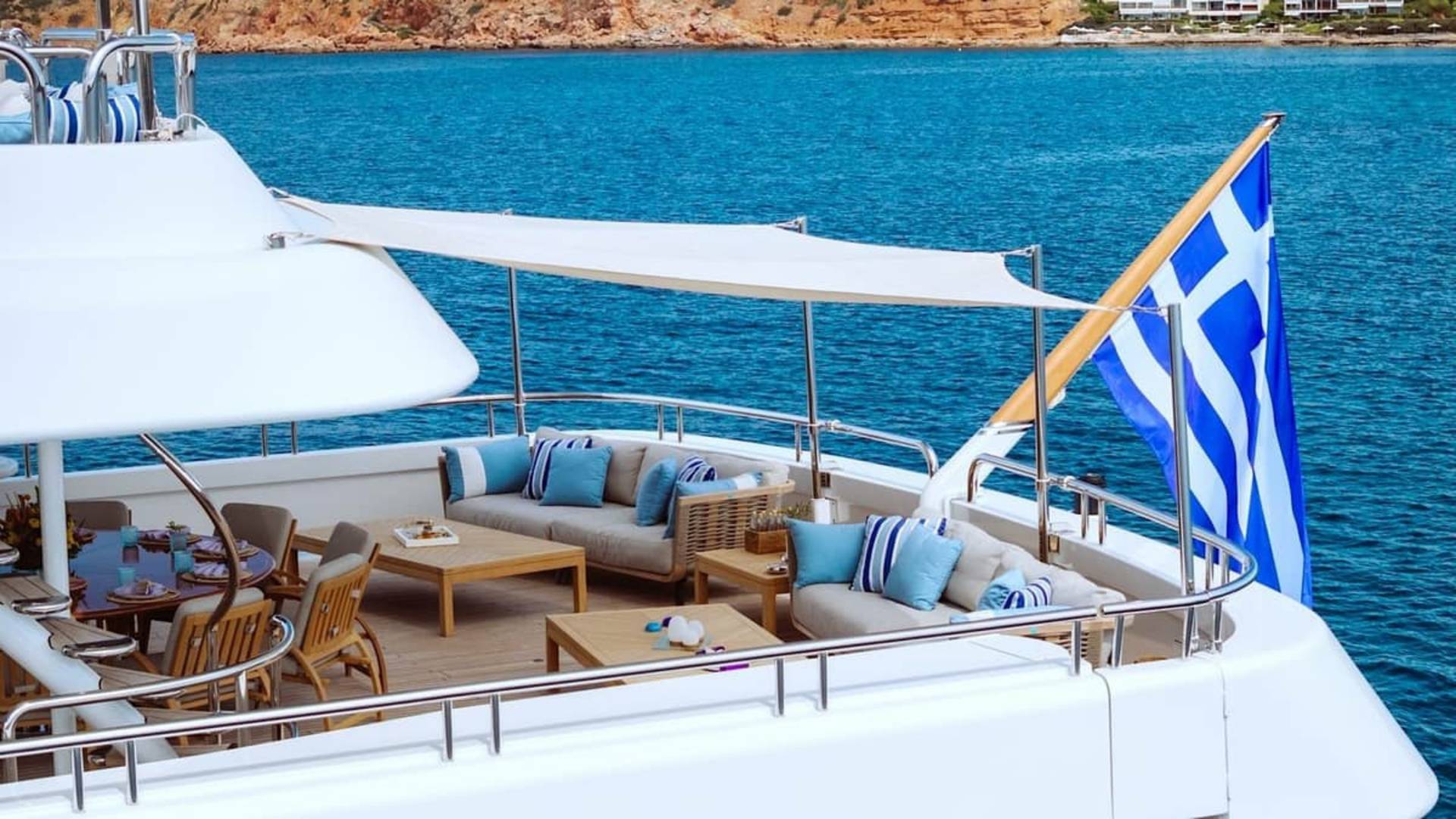 A luxurious yacht with a Greek flag and comfortable seating area cruises through the azure waters of Greece.
