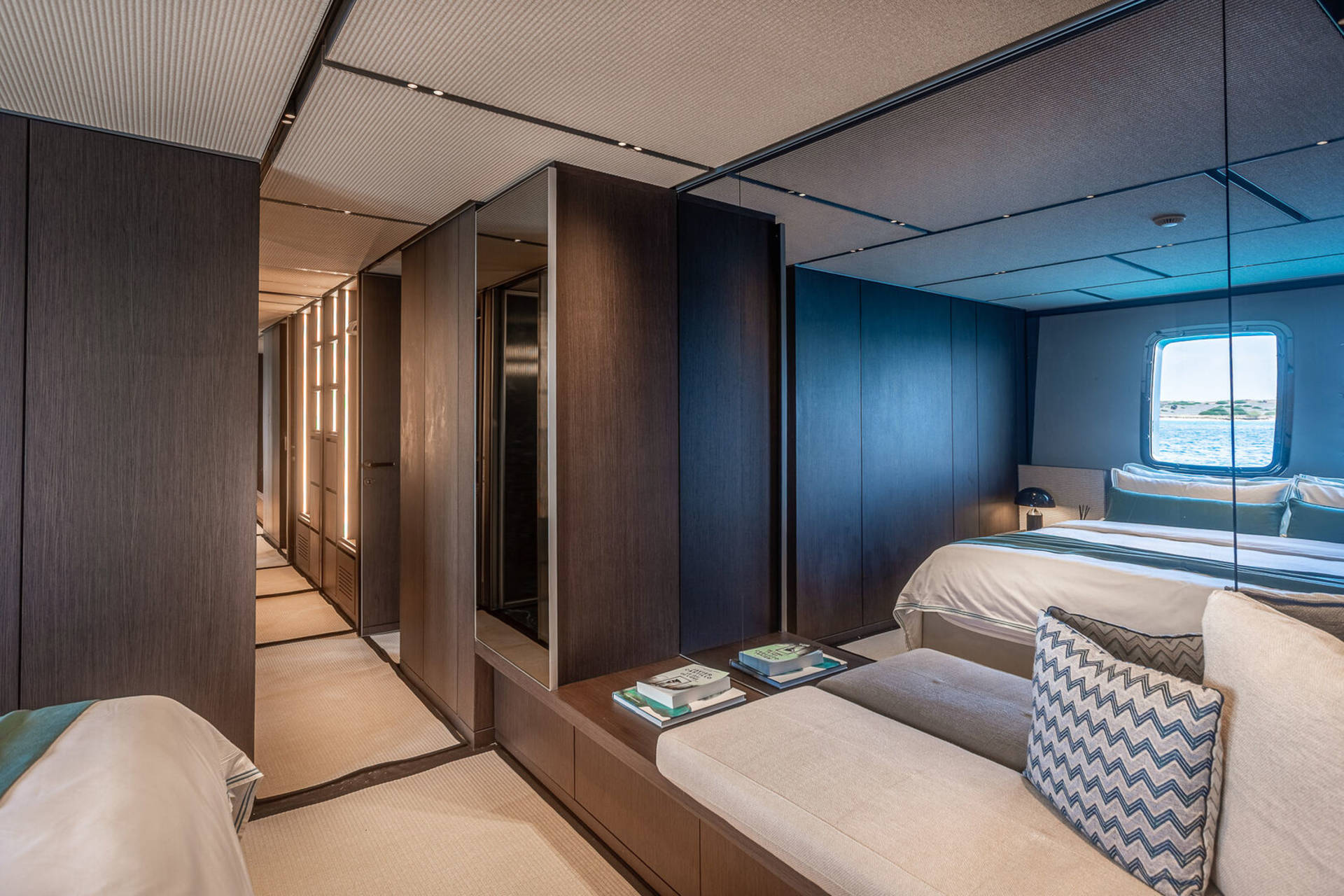 A luxurious yacht cabin offers a serene retreat with a view of the sparkling sea through a porthole window.