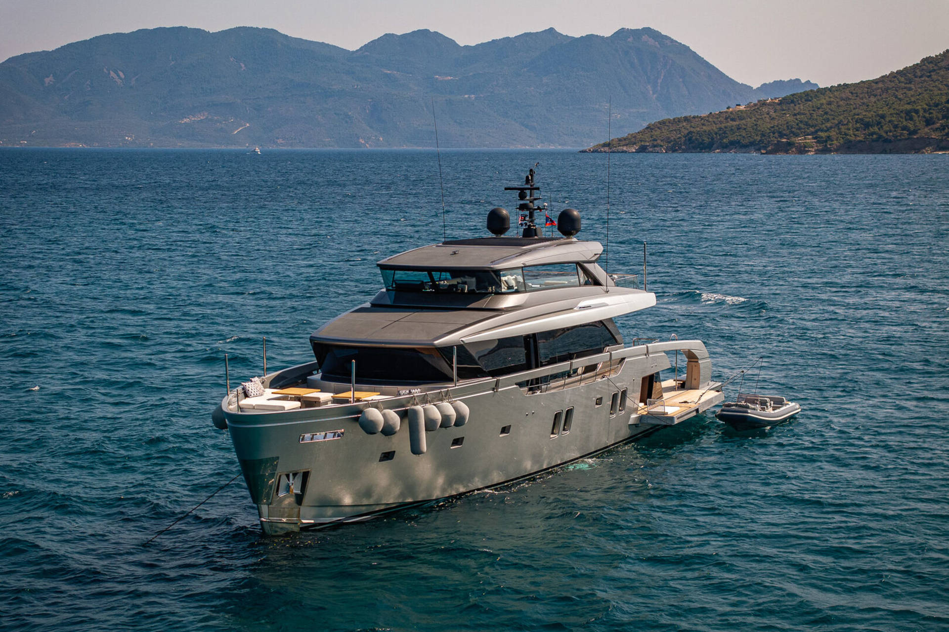 A sleek, modern yacht anchors in the azure waters off a verdant, mountainous coastline.