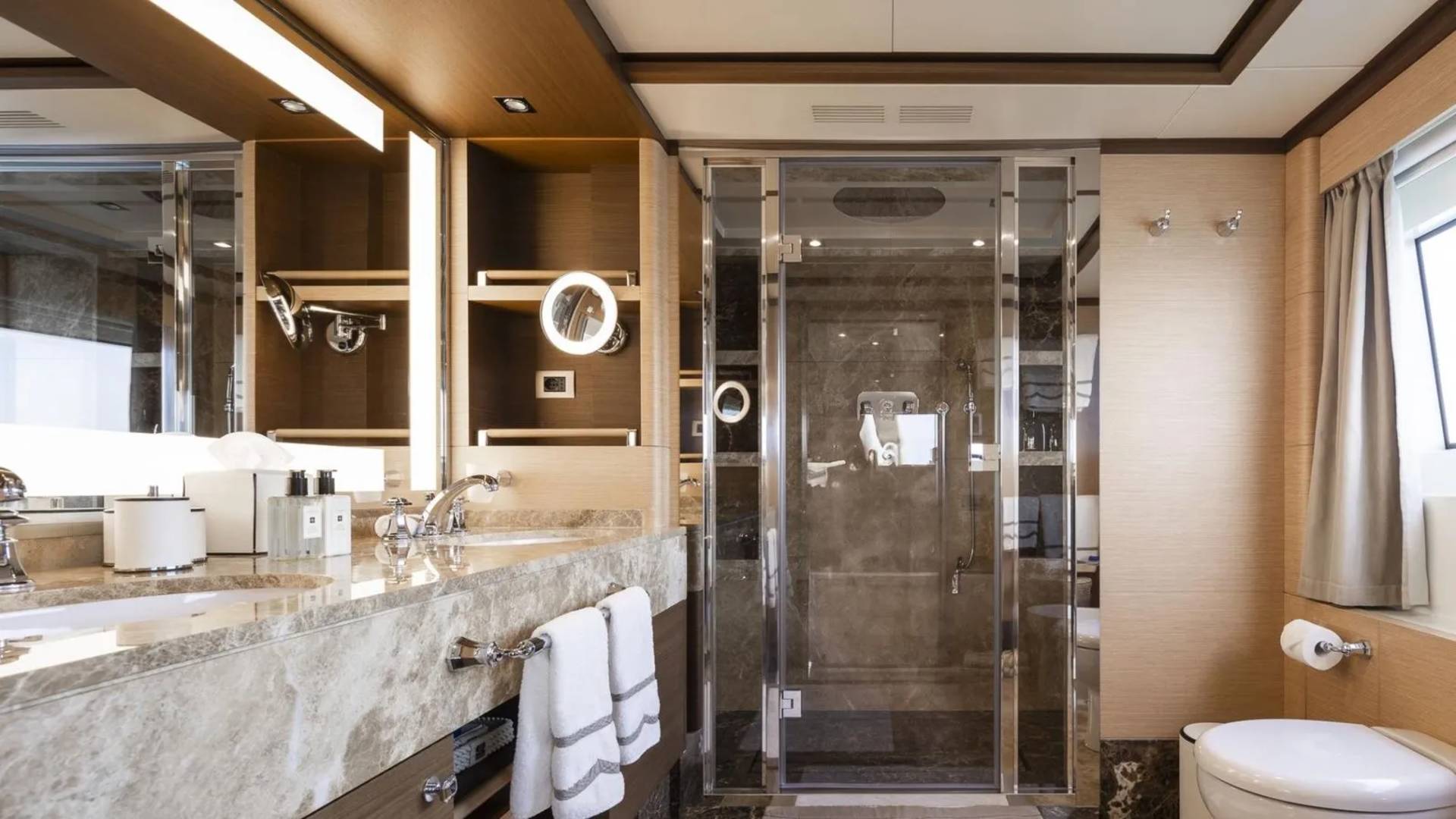 Luxurious yacht bathroom features a marble vanity, glass-enclosed shower, and elegant wood finishes.