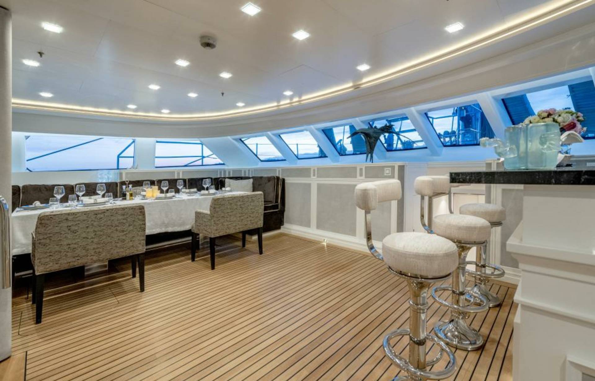 Elegant bar stools and a formal dining table await guests on this luxurious yacht's sunlit deck.