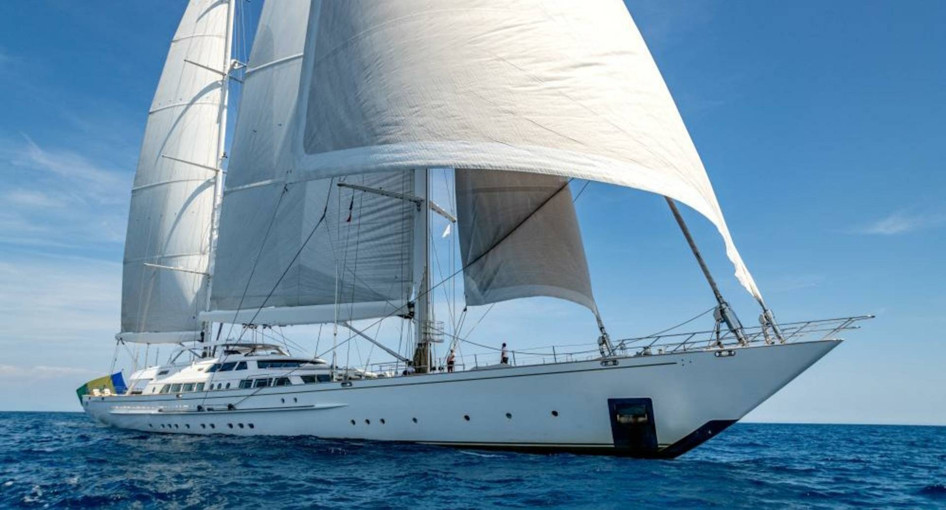 A majestic white sailing yacht glides across the deep blue ocean under a clear sky.