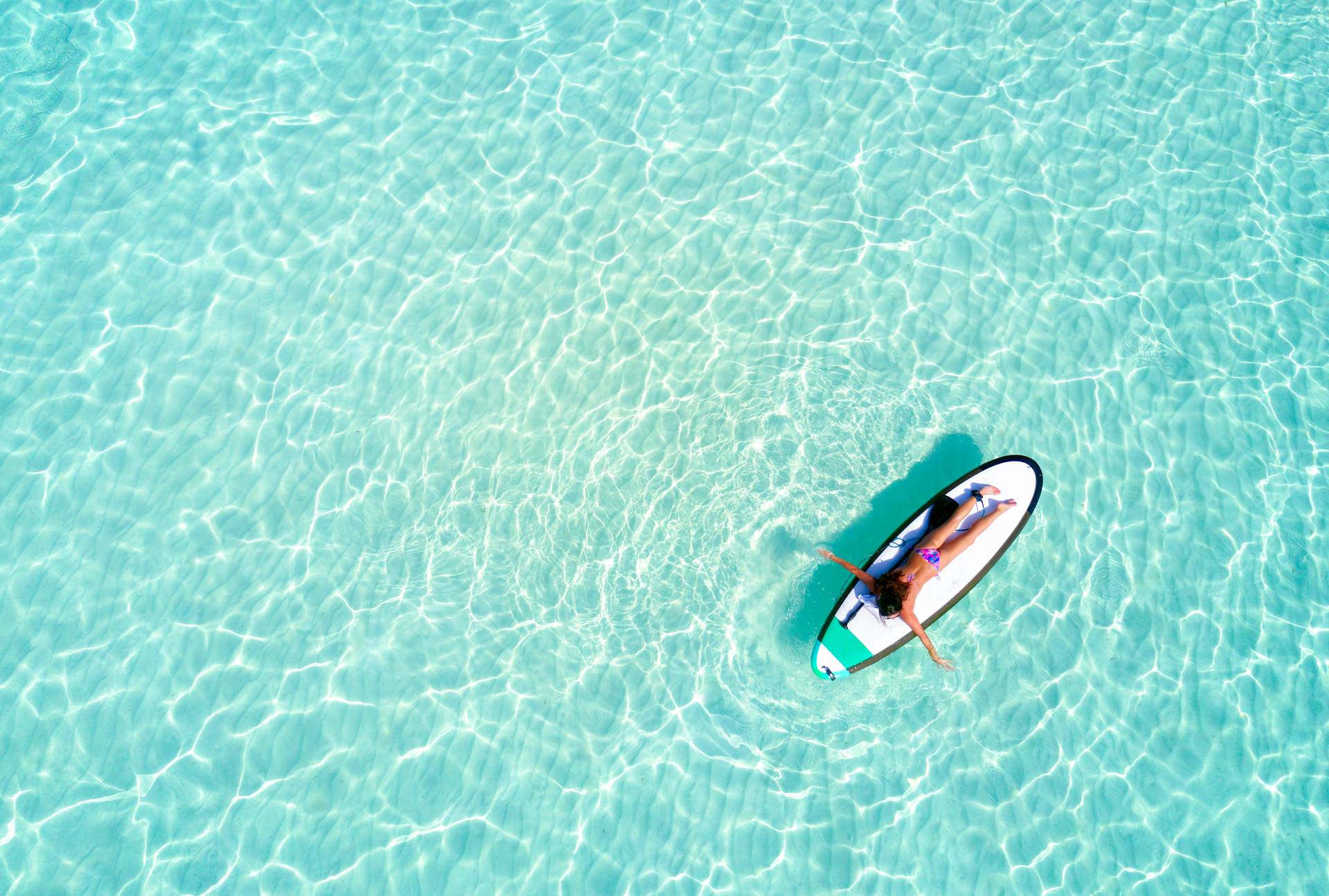 A woman relaxes on a paddleboard in crystal-clear turquoise waters, enjoying the sun and gentle waves.