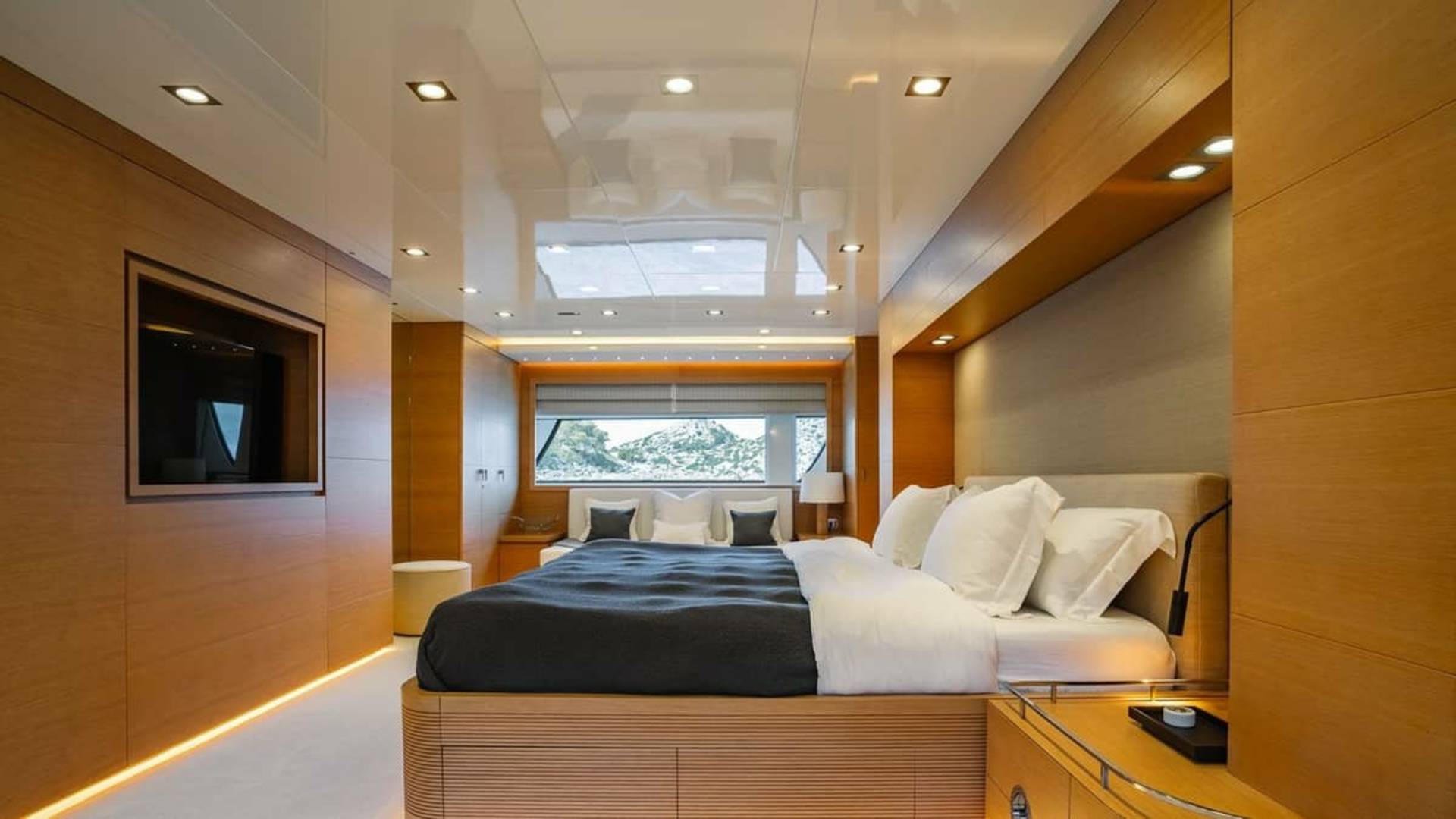 Luxurious yacht interiors feature warm wood paneling and a plush king-sized bed with a scenic view.