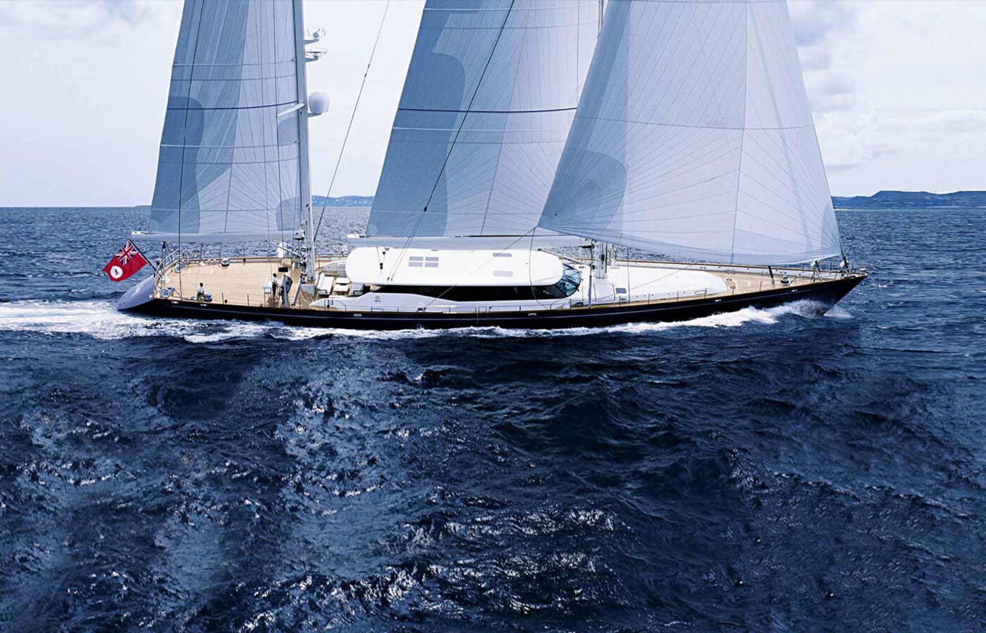 A majestic sailing yacht glides through the deep blue ocean under a cloudy sky.