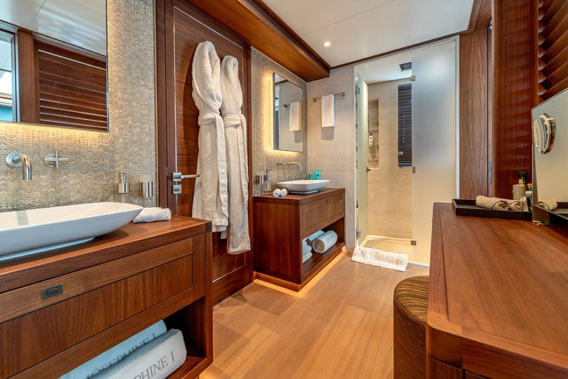 Luxurious white bathrobes hang on a wooden door in this elegant yacht bathroom.