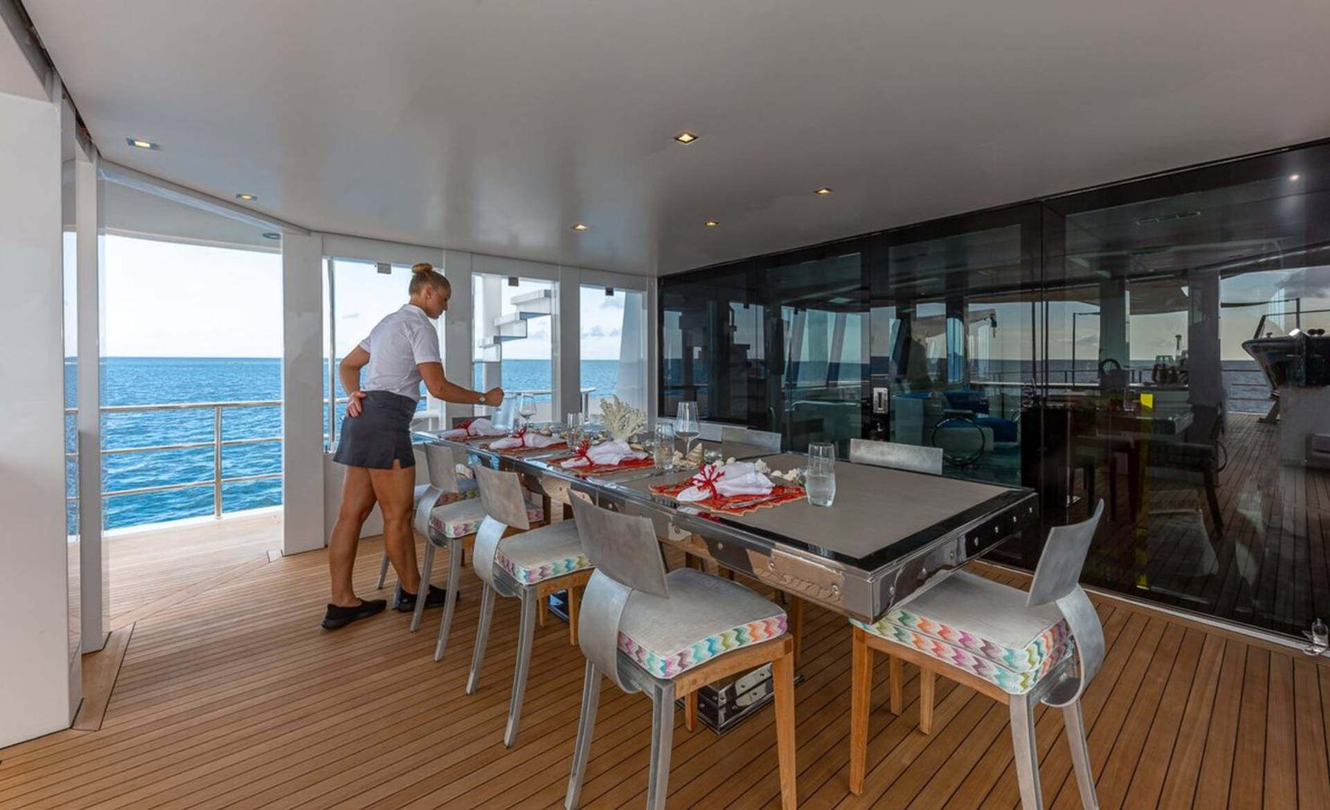 A server sets a formal dining table on a yacht's deck with the ocean as a backdrop.