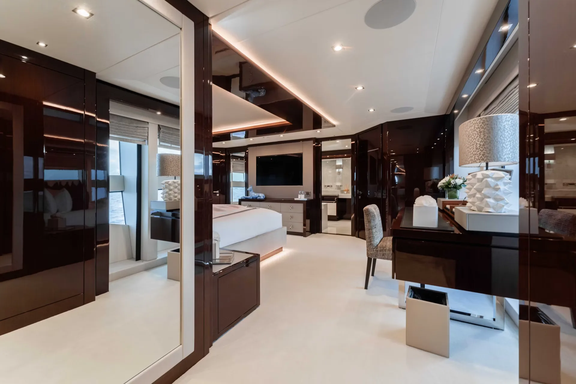 Luxurious yacht interiors feature a spacious bedroom with a king-sized bed, a large television, and a vanity area.