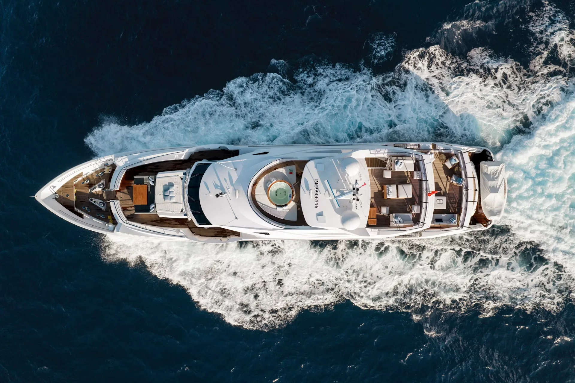 A large, luxurious yacht navigates through the choppy, dark blue waters, surrounded by a dramatic, rocky coastline.