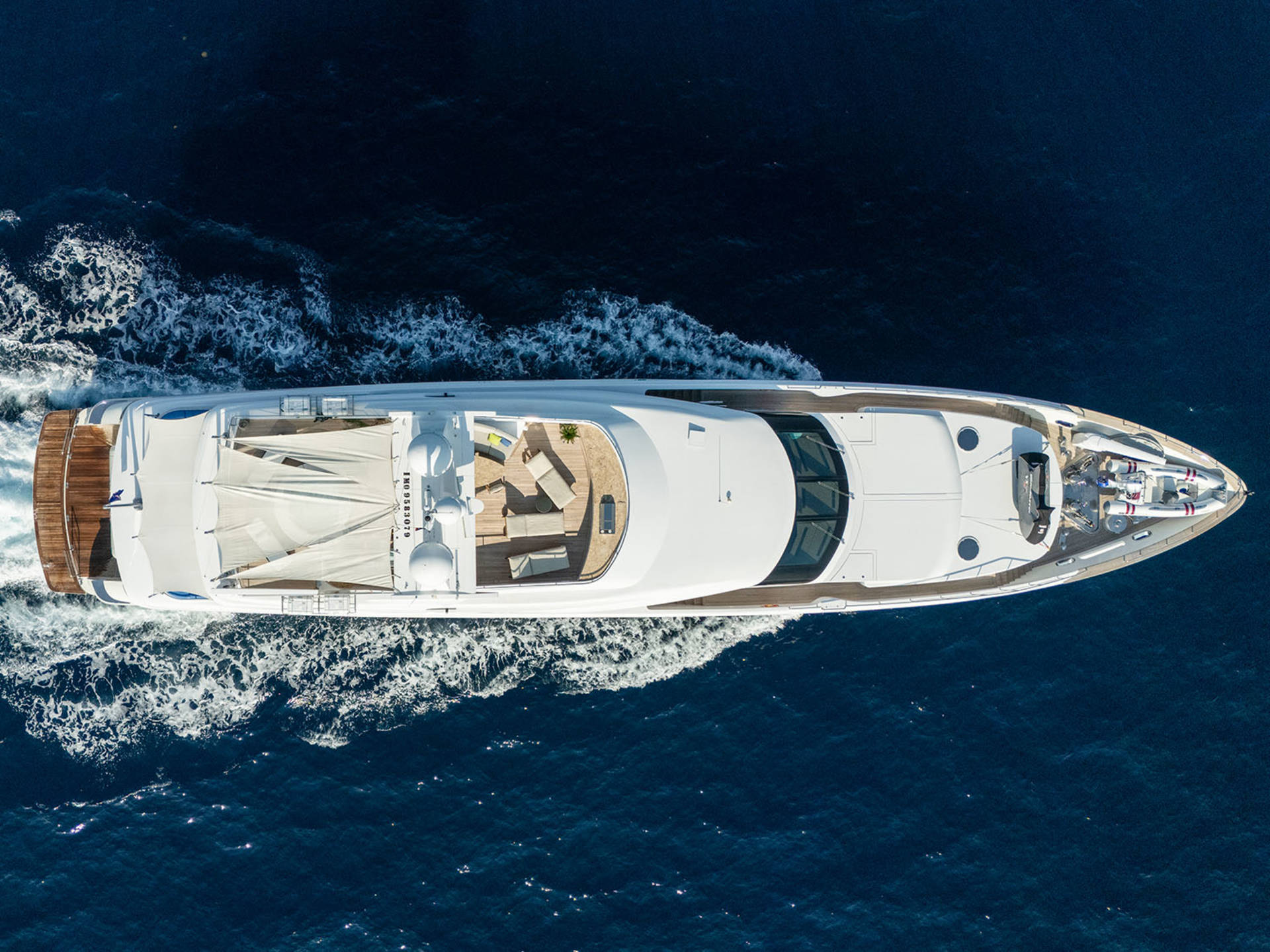 A sleek white yacht glides through the deep blue ocean, leaving a trail of white foam in its wake.