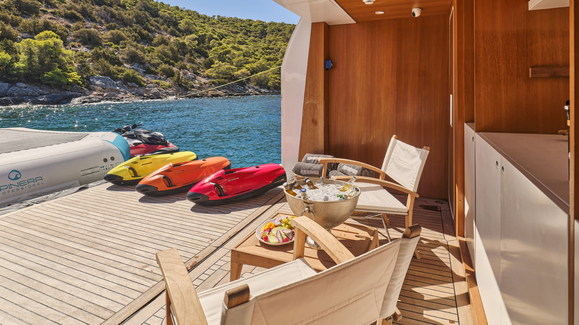 A wooden deck overlooking a scenic turquoise bay, with colorful kayaks and a cozy seating area in the foreground.