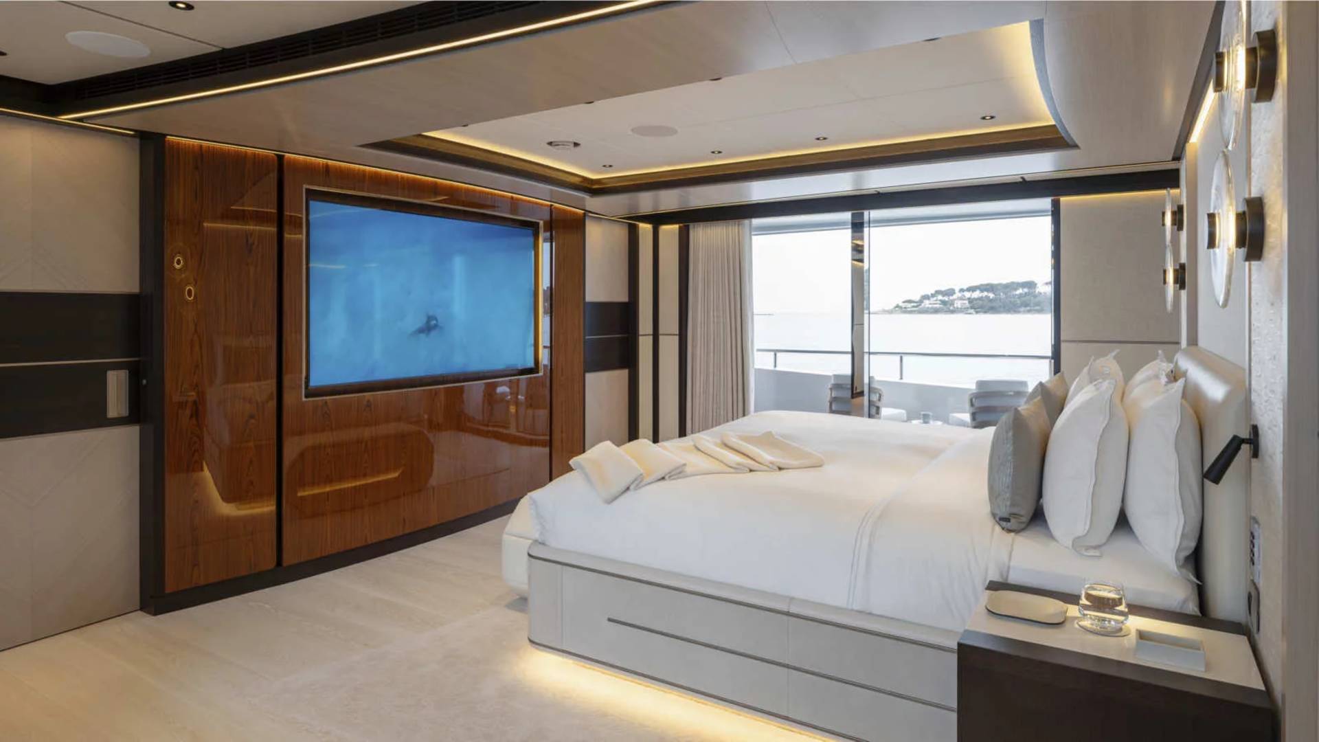 Luxurious yacht bedroom offers a stunning view of the ocean through expansive windows, complemented by a large television screen.