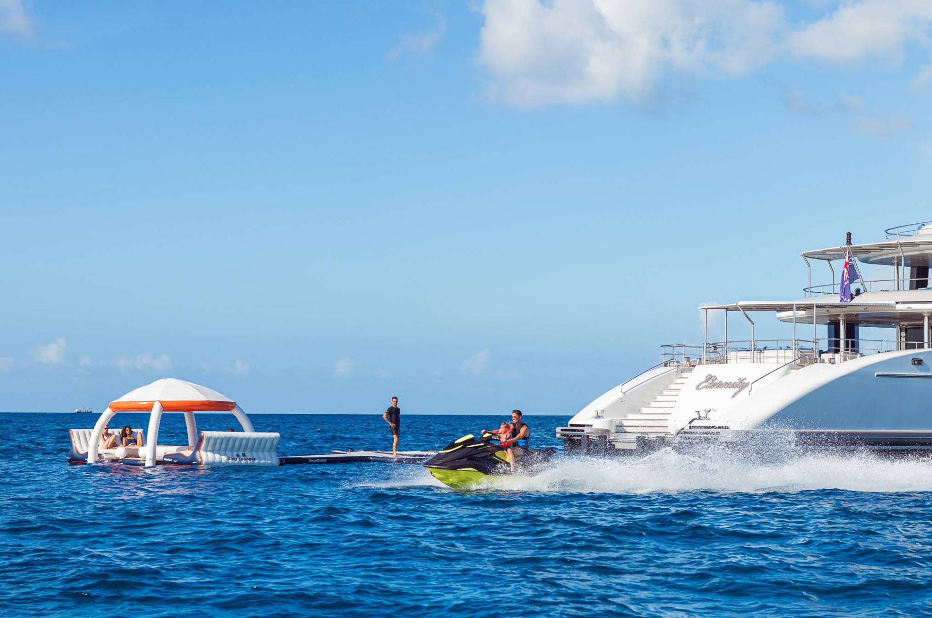 A jet ski speeds through turquoise waters near a luxurious yacht and a floating lounge.