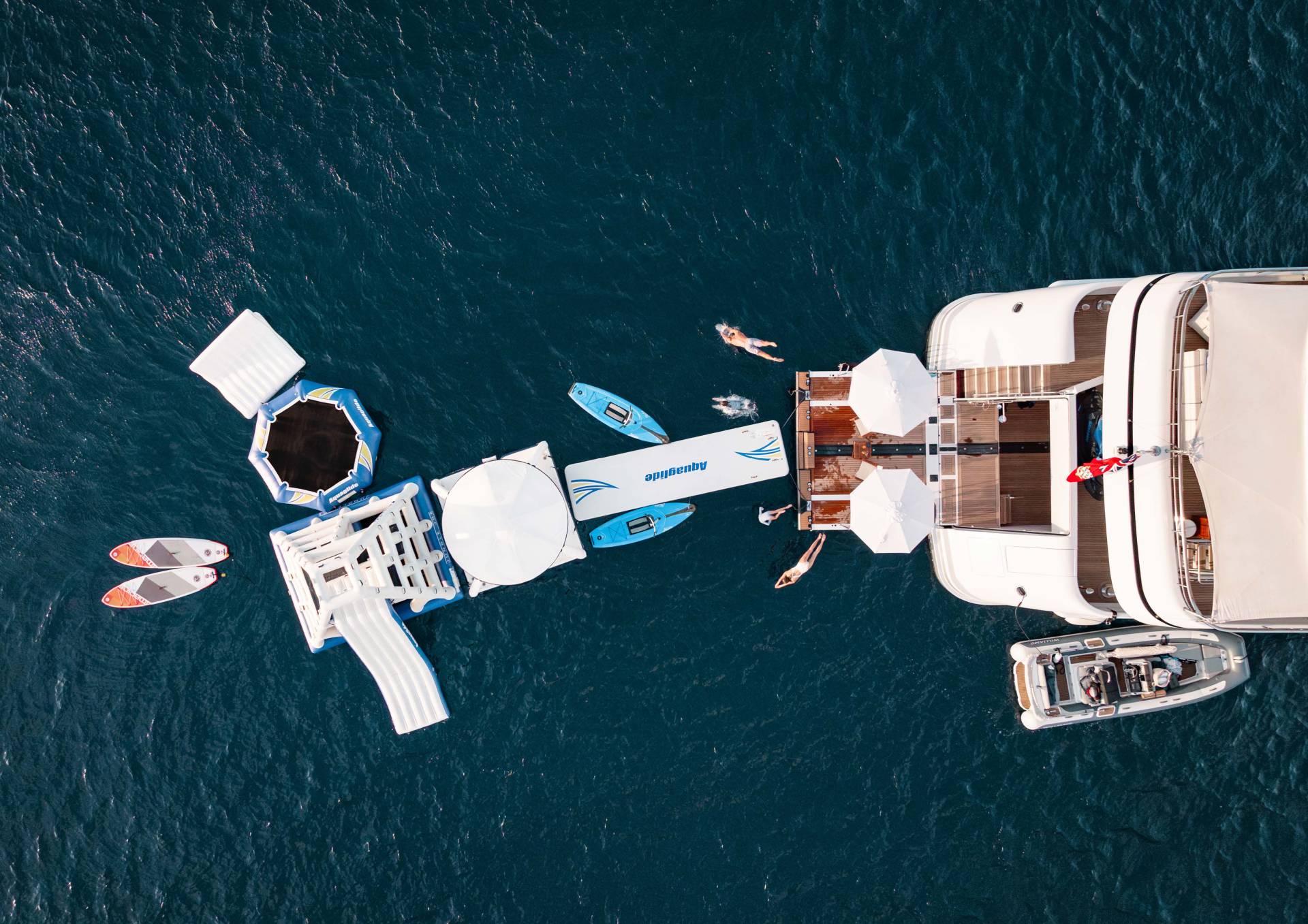 People enjoy a sunny day of water sports and relaxation near a luxurious yacht anchored in the clear blue sea.