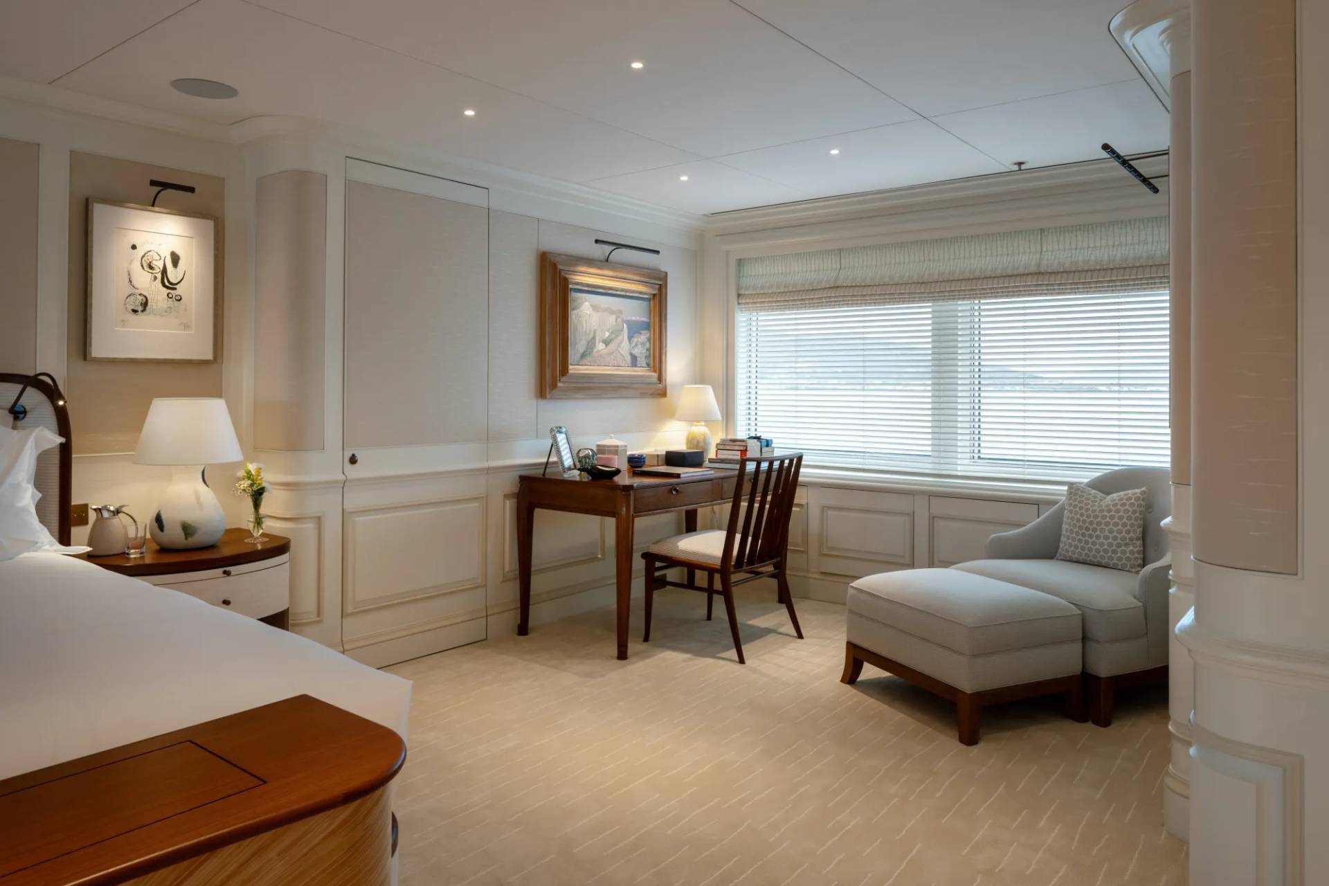 A cozy and well-furnished bedroom with a desk, chair, and a comfortable armchair near the window, creating a warm and inviting atmosphere.