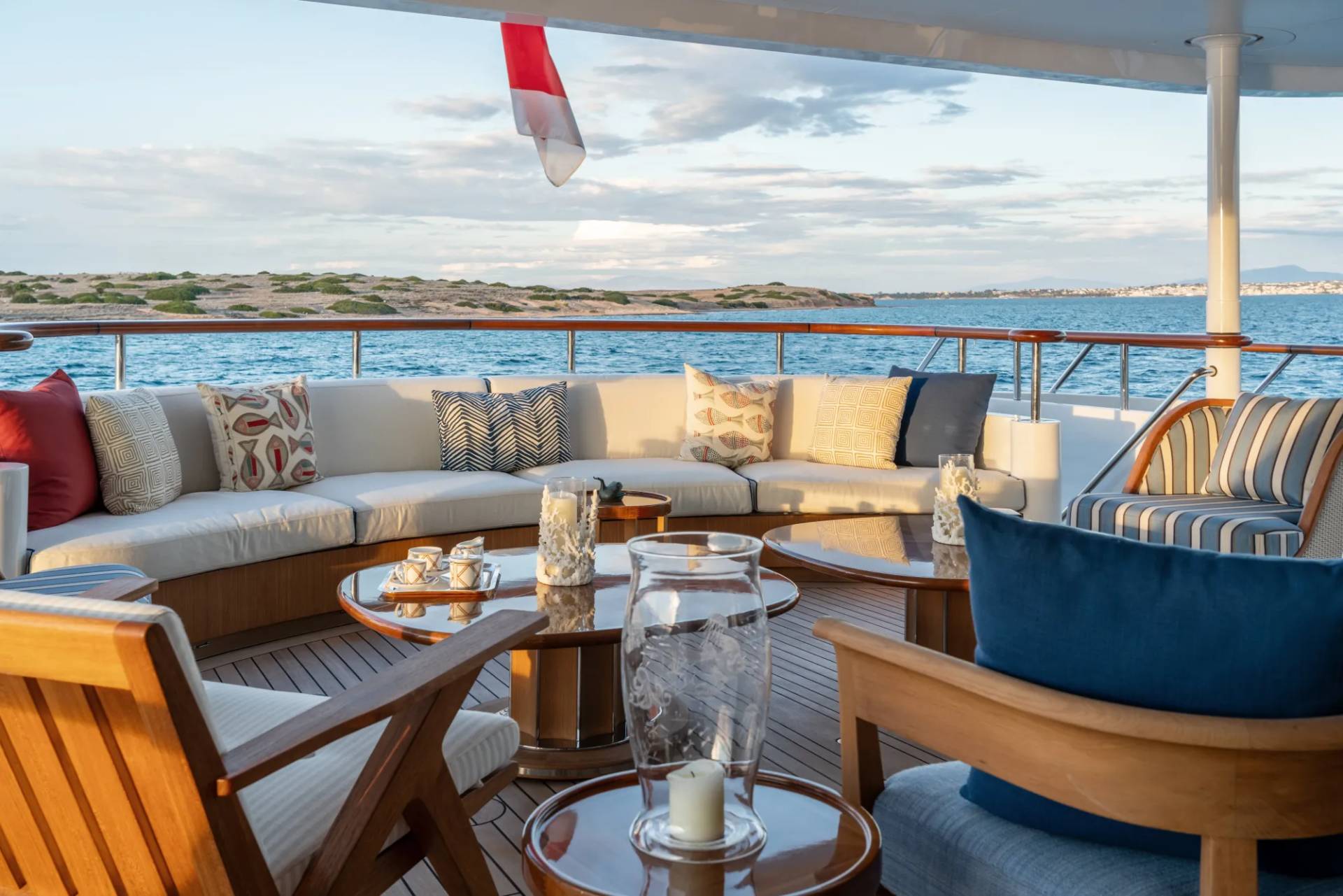 A cozy outdoor seating area on a boat or yacht, with plush cushions and a scenic view of the ocean and coastline in the background.