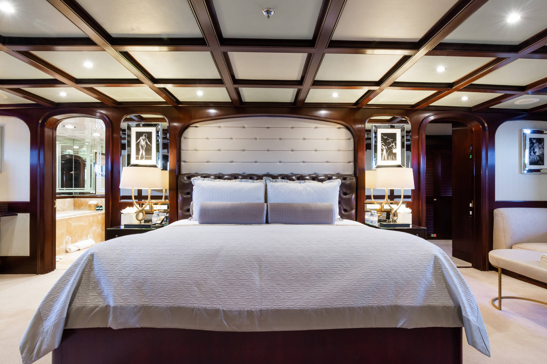 A luxurious bedroom with a large bed in the foreground and ornate wooden paneling and doorways in the background.