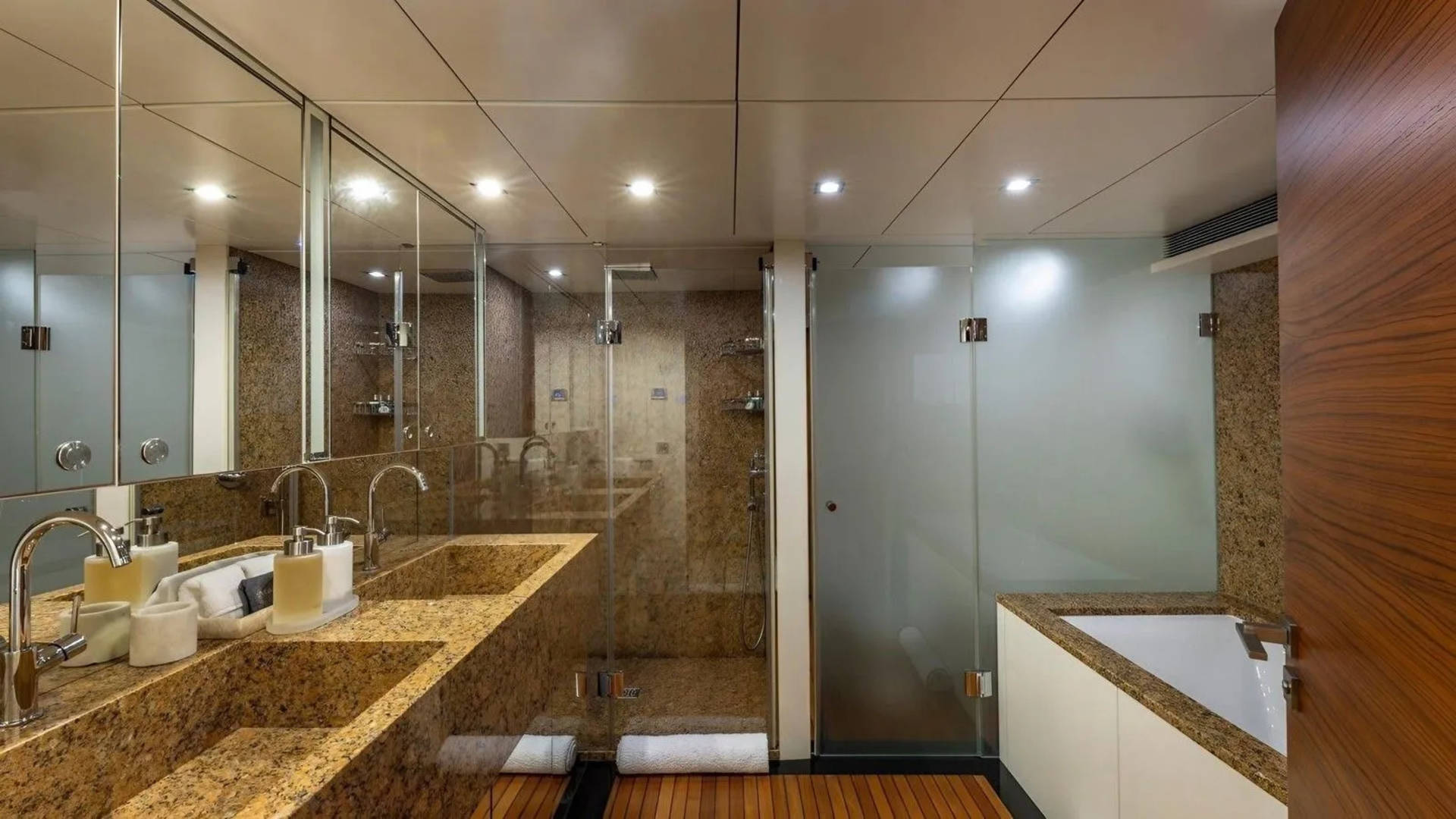 A modern bathroom with a double vanity in the foreground and a glass-enclosed shower and bathtub in the background.