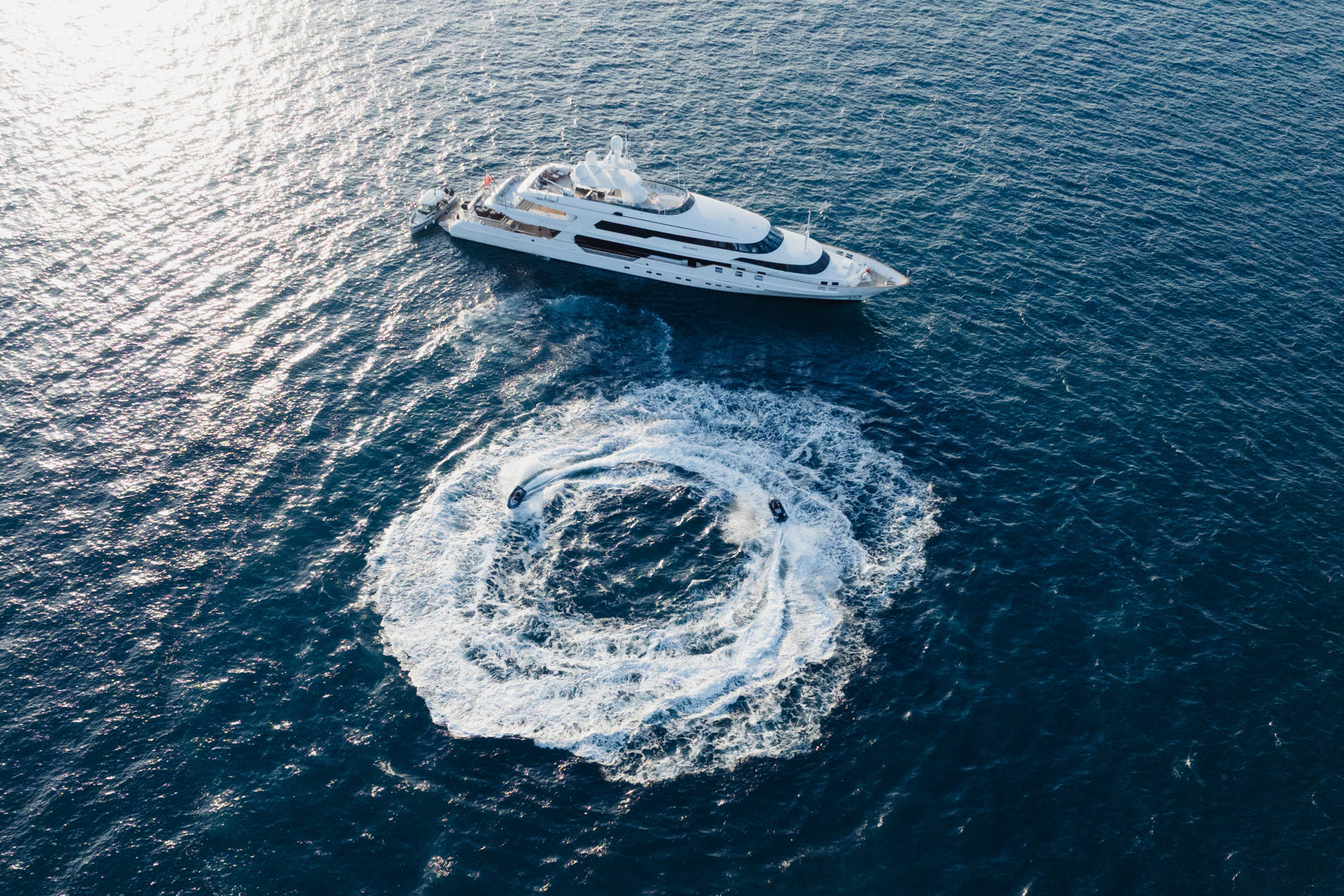 A large white yacht cruises on a deep blue ocean, leaving a circular wake in its path.
