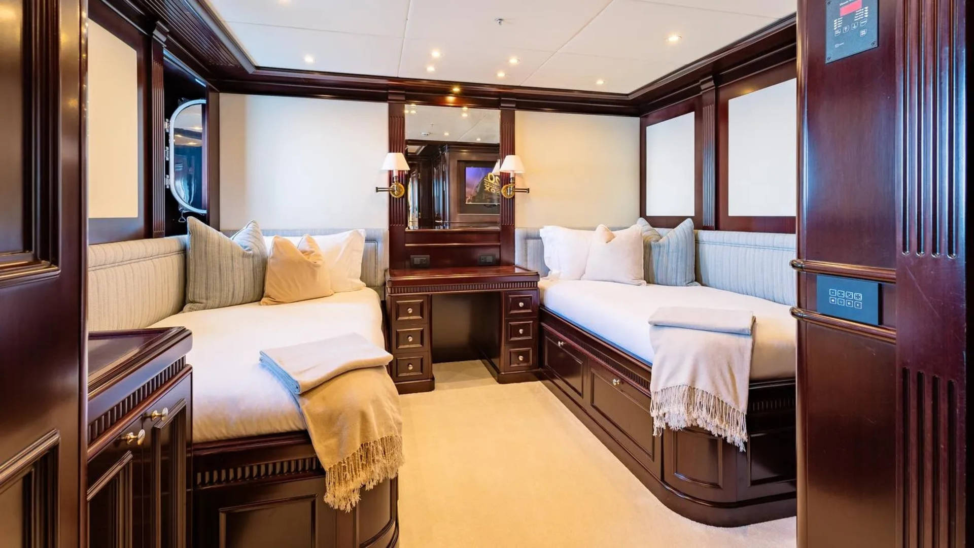 Two beds with plush pillows and blankets are in the foreground, while a vanity with mirrors and ornate wooden paneling fills the background of this luxurious cabin.