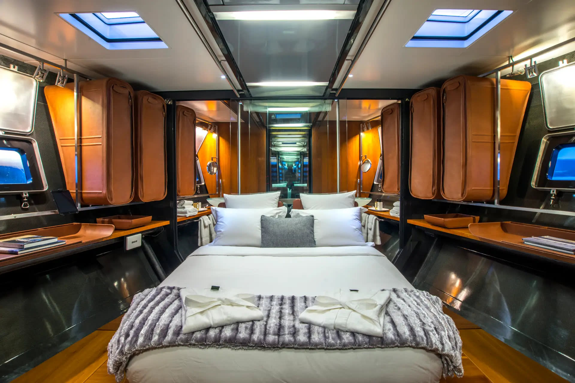 A luxurious bedroom with a plush bed in the foreground and mirrored walls reflecting the room's modern design in the background.