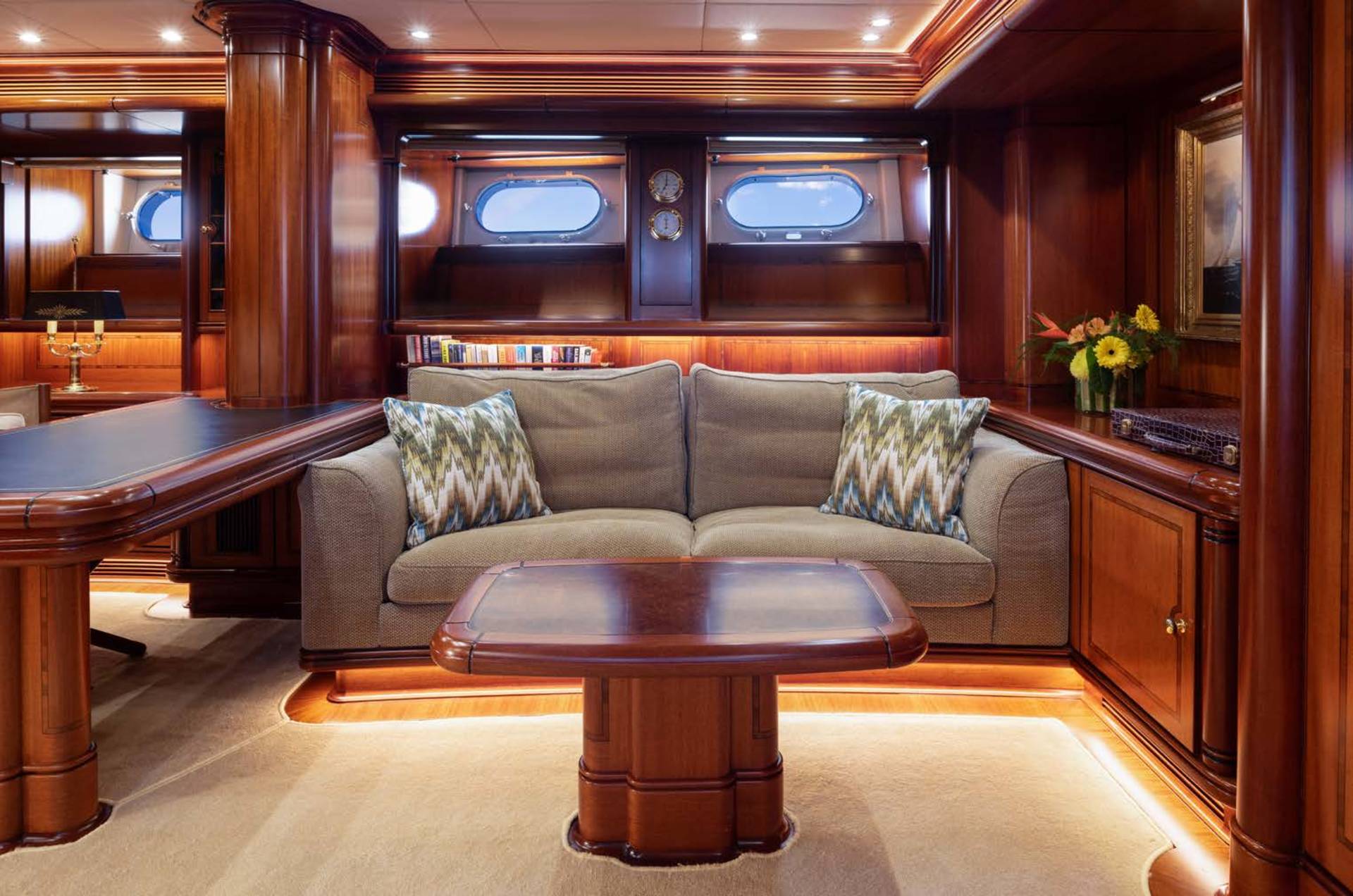 A plush sofa with decorative pillows sits in the foreground of a luxurious wood-paneled room with oval windows in the background.