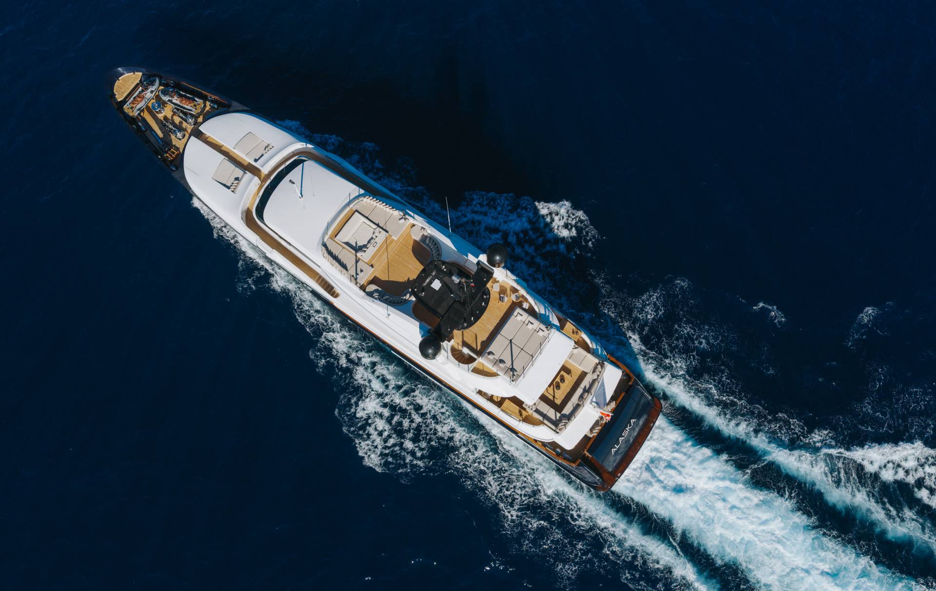 A luxury yacht cruises through deep blue ocean waters, leaving a trail of white foam in its wake.