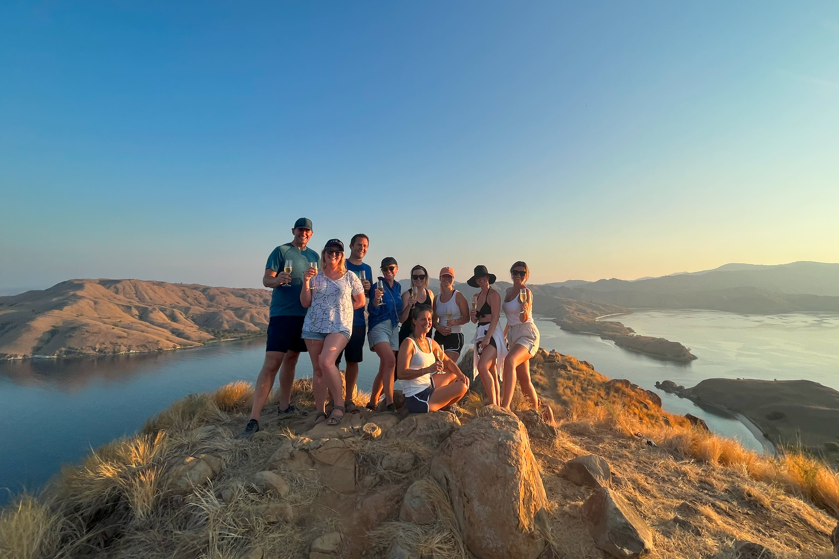 A group of friends enjoys a celebratory toast on a sun-drenched hilltop overlooking a serene bay.