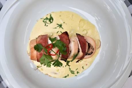 A beautifully plated dish features chicken wrapped in prosciutto, served in a creamy sauce with fresh herbs and a hint of chili.