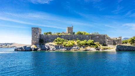 The ancient stone walls of Bodrum Castle stand majestically against a brilliant blue sky, overlooking the sparkling Aegean Sea.