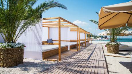 Relax in shaded cabanas on a sandy beach with a view of the turquoise sea and bustling crowds.