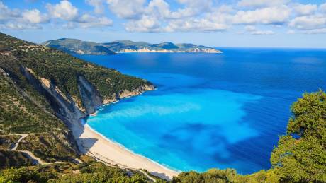 A winding road leads to the stunning turquoise waters and white sand beach of Myrtos Bay on Kefalonia, Greece.