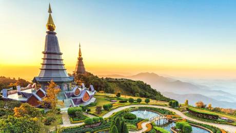 Golden sunrise illuminates twin pagodas and a vibrant garden overlooking misty mountain layers.