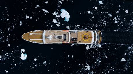 An aerial view captures a luxury yacht navigating through a sea dotted with ice floes.