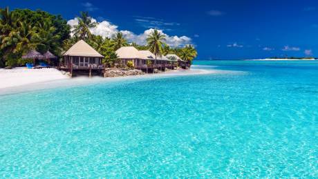 Overwater bungalows nestle on a pristine white sand beach beside the impossibly turquoise waters of a tropical paradise.
