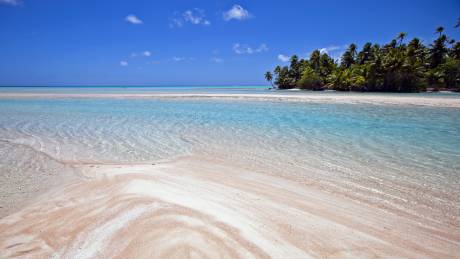 A pristine sandy shore meets the crystal-clear turquoise waters of a tropical paradise under a brilliant blue sky.