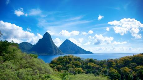 The majestic Pitons rise from the turquoise waters of St. Lucia, framed by lush green foliage under a brilliant blue sky.