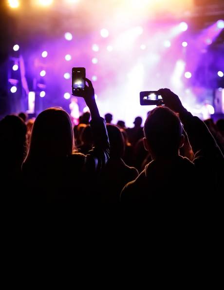 Concertgoers capture the vibrant stage lights and energetic atmosphere with their phones.