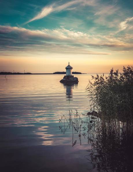 A solitary lighthouse stands on a rocky outcrop in calm waters under a dramatic sunset sky.
